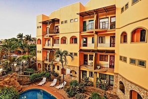 A multi-story hotel with balconies, a swimming pool, and lush landscaping. - Pura Vida Dreams (Tamarindo)
