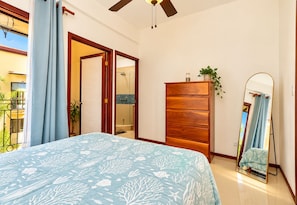 A bedroom with a bed, a wooden dresser, a mirror, and a sliding glass door leading to a balcony. - Pura Vida Dreams (Tamarindo)