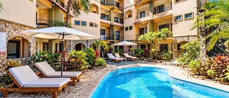 A hotel pool area with lounge chairs, a swimming pool, and a stone wall.