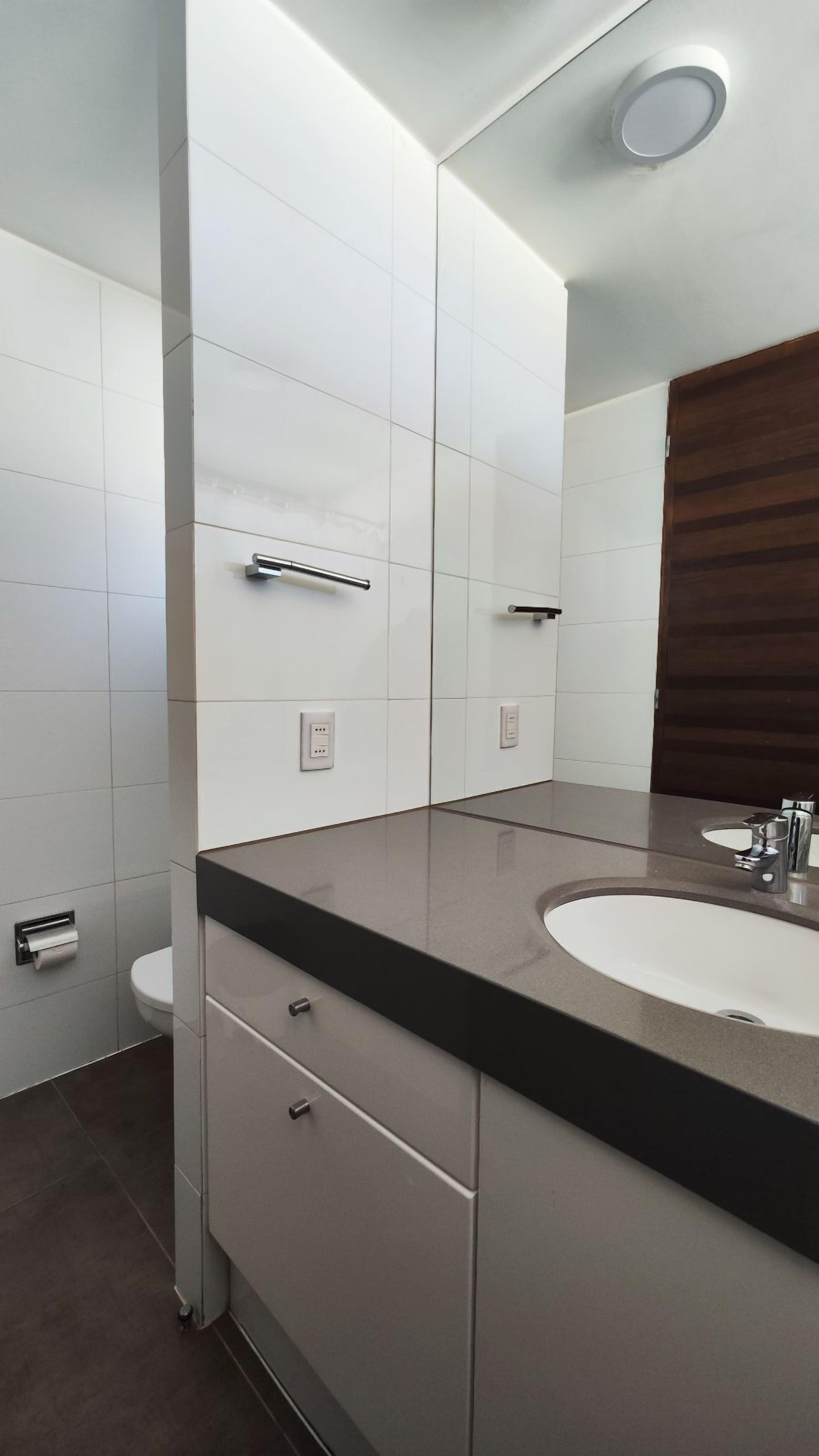 Un baño moderno con un espejo grande, un lavabo y un inodoro.