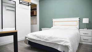 Un dormitorio con cama, mesitas de noche, un tocador, un espejo y un armario.