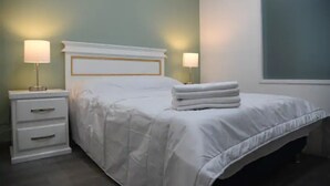 Una cama bien tendida con edredón blanco y almohadas, dos mesitas de noche con lámparas y una ventana con vistas.