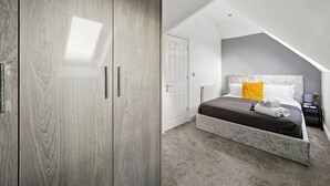 A bedroom with a sloped ceiling, a bed with a marble headboard, a grey wardrobe, and a white door.