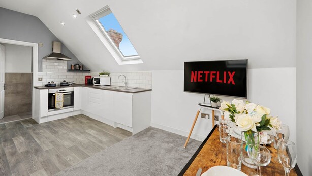 A modern kitchen with a built-in oven, microwave, and sink. A large TV screen displays the Netflix logo.