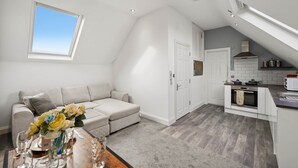 A modern loft apartment with a dining area, a kitchenette, and a living space with a sofa and a window.