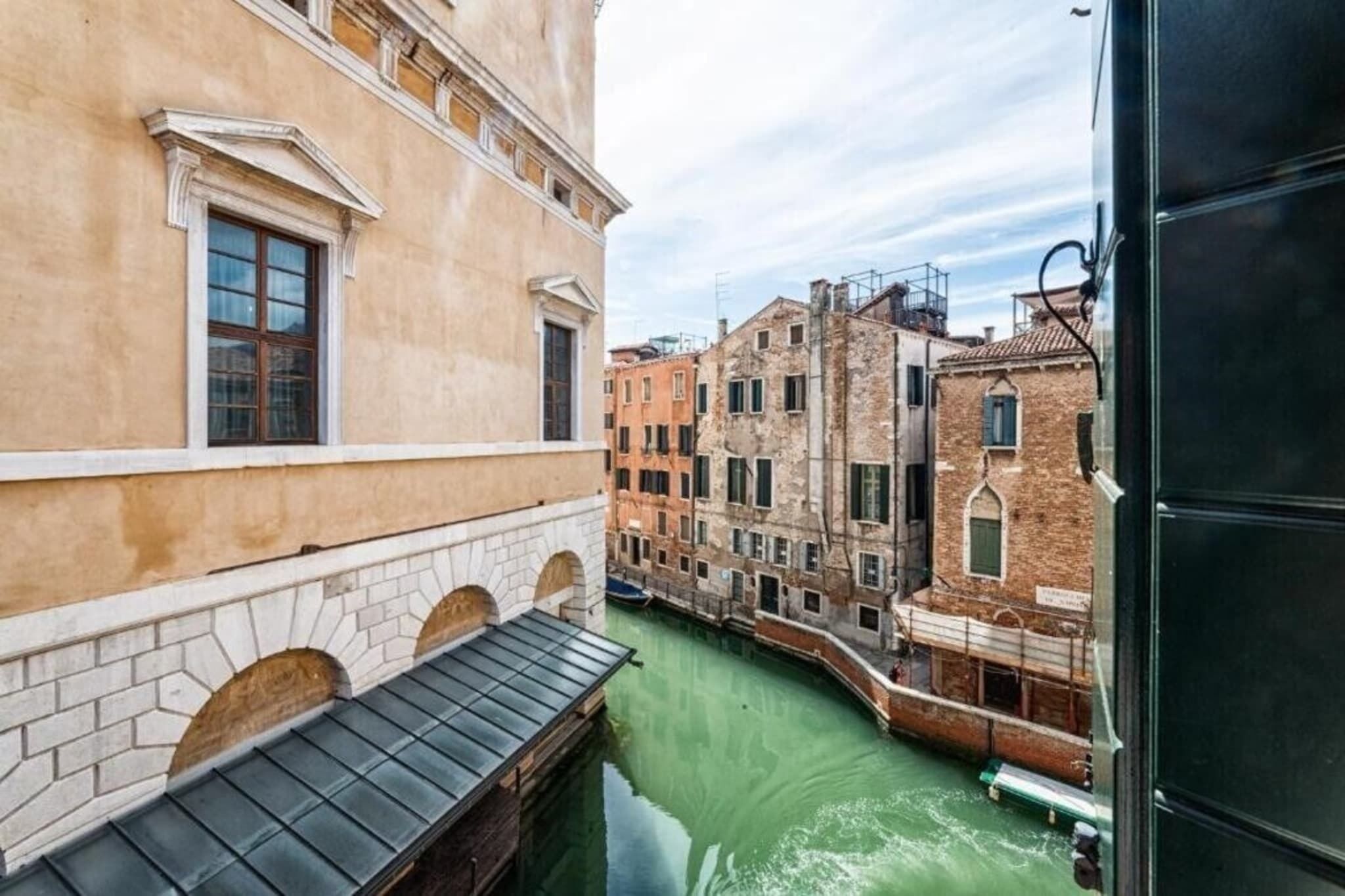 A narrow canal with buildings on either side, featuring arched windows and a mix of brick and plaster facades.