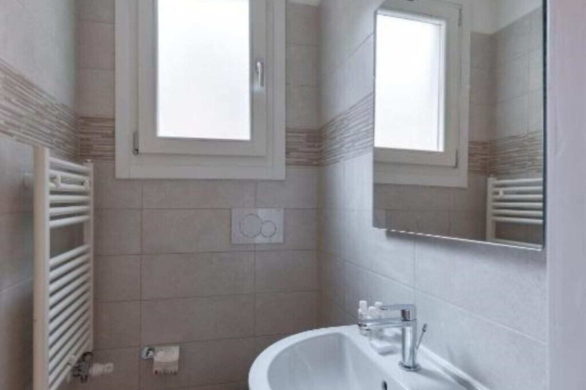 Un baño con un lavamanos blanco, un espejo y una ventana.