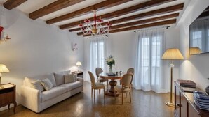 A cozy living room with a sofa, a dining table with chairs, a chandelier, and a lamp. - Casanova Fenice III (Venezia)