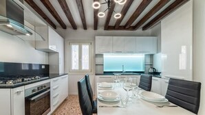 A modern kitchen with white cabinets, a black countertop, and a dining area with a table set for four. - Casanova Fenice III (Venezia)
