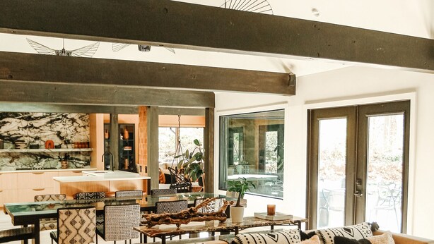 A spacious living area with a large sofa, coffee table, and pendant lights. A kitchen is visible in the background with a large window.
