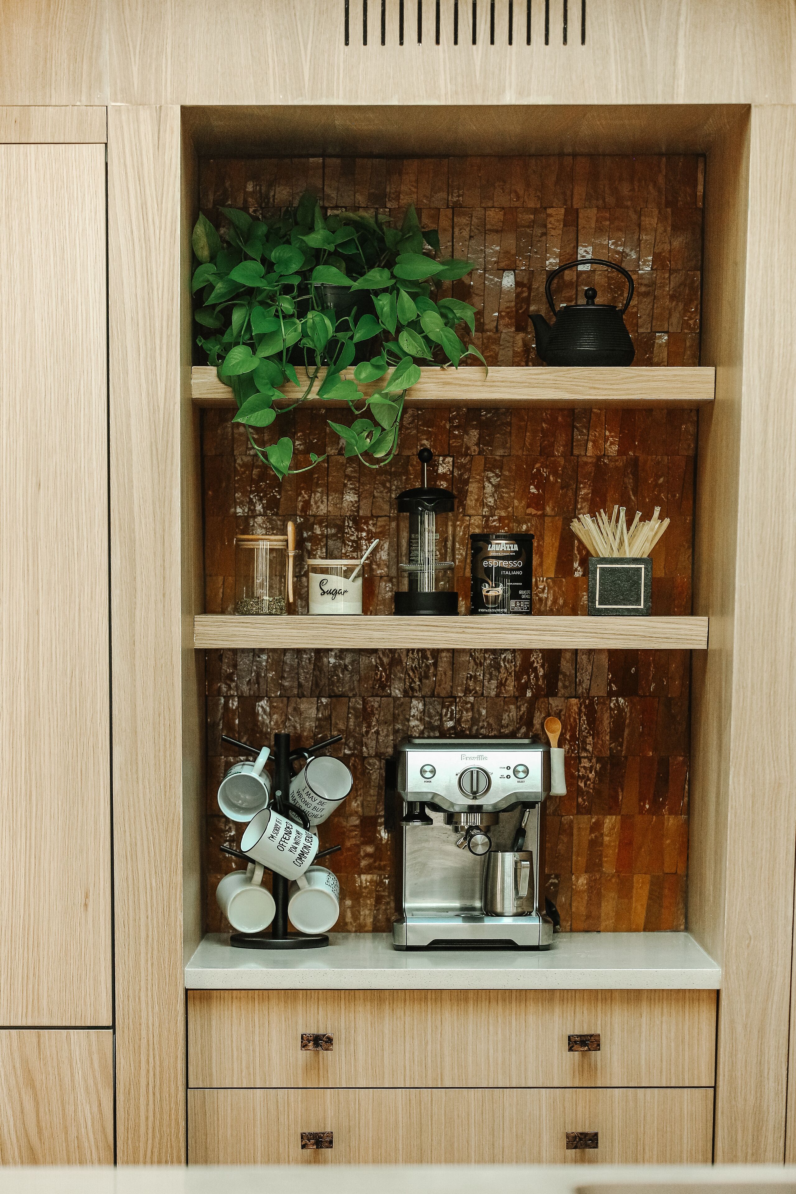 A kitchen with wooden cabinets, a coffee machine, a kettle, and a plant on the shelves.