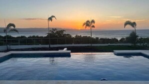 A swimming pool with a sunset view, palm trees, and a fence. - Luxury Beach Front Villa with Private pool and stunning Ocean View! (Punta Rucia)