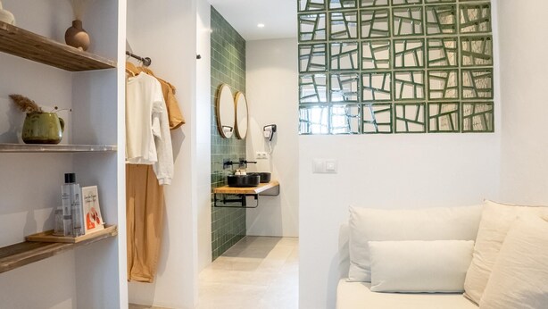 A modern bathroom with a shower, a sink, and a mirror. There is a towel rack with towels and a shelf with toiletries.