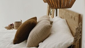 A neatly made bed with a wooden headboard, a woven lamp, and a vase with dried plants. - Salina Deluxe with balcony Room (Vejer de la Frontera)