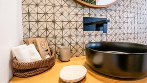 A bathroom with a modern sink, a mirror, a towel, a cup, and a decorative wall. - Salina Deluxe with balcony Room (Vejer de la Frontera)