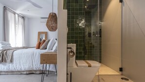 A modern bedroom with a bed, bedside table, and a large window. Adjacent to the bedroom is a bathroom with a toilet, shower, and green-tiled walls. - Salina Deluxe with balcony Room (Vejer de la Frontera)