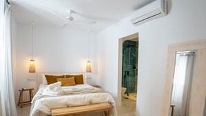 Une chambre à coucher comprenant un lit, des lampes de chevet, un ventilateur de plafond, un appareil de climatisation et un banc en bois.