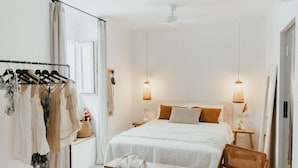 Une chambre à coucher au style minimaliste, comprenant un lit, des tables de chevet, une chaise, un luminaire suspendu et un portant à vêtements.