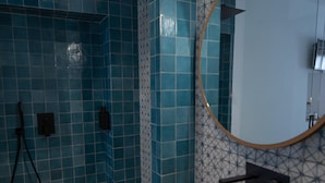 A bathroom with blue-tiled walls, a wooden bench, a round mirror, and a shower area.