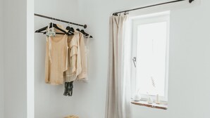 A minimalist bathroom with a wooden stool, a potted plant, and a clothing rack with beige garments.
