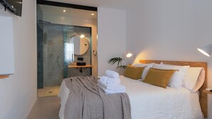 A modern hotel room with a large bed, a bedside table, a mirror, and a bathroom with a glass door.