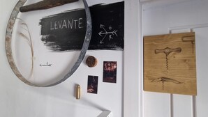 A wall with a circular metal object, a blackboard with 'LEVANTE' written on it, a wooden board with a drawing, and a small gold bottle.