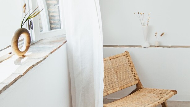 Une pièce comprenant une chaise en osier, un objet décoratif en bois et une étagère avec des vases et des plantes séchées.