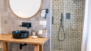Une salle de bain avec un miroir rond, un lavabo noir, un tabouret en bois et une douche aux carreaux décorés.