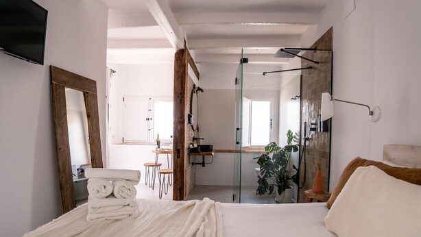 A modern bedroom with a large bed, a glass shower enclosure, and a small seating area with a table and chairs.