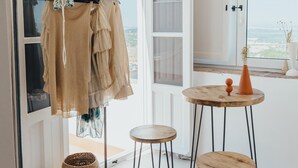 A room with a clothing rack, a small round wooden table with a vase, and a view of the outdoors through a window.
