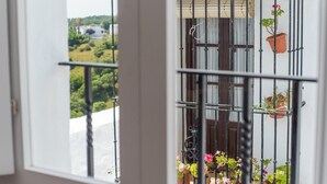 Un balcón con barandilla de metal, plantas en macetas y vistas a zonas verdes y edificios.