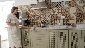 Una cocina con baldosas estampadas, cafetera, tetera y un lavamanos.