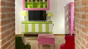 A room with a green and white striped bench, a pink table, a green chair, and a red chair. - Jesuit Apartment (Venezia)