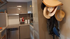 Une cuisine moderne équipée d’appareils électroménagers en acier inoxydable, d’une machine à café et d’un porte-chapeaux mural où sont accrochés des chapeaux et un sac bleu.