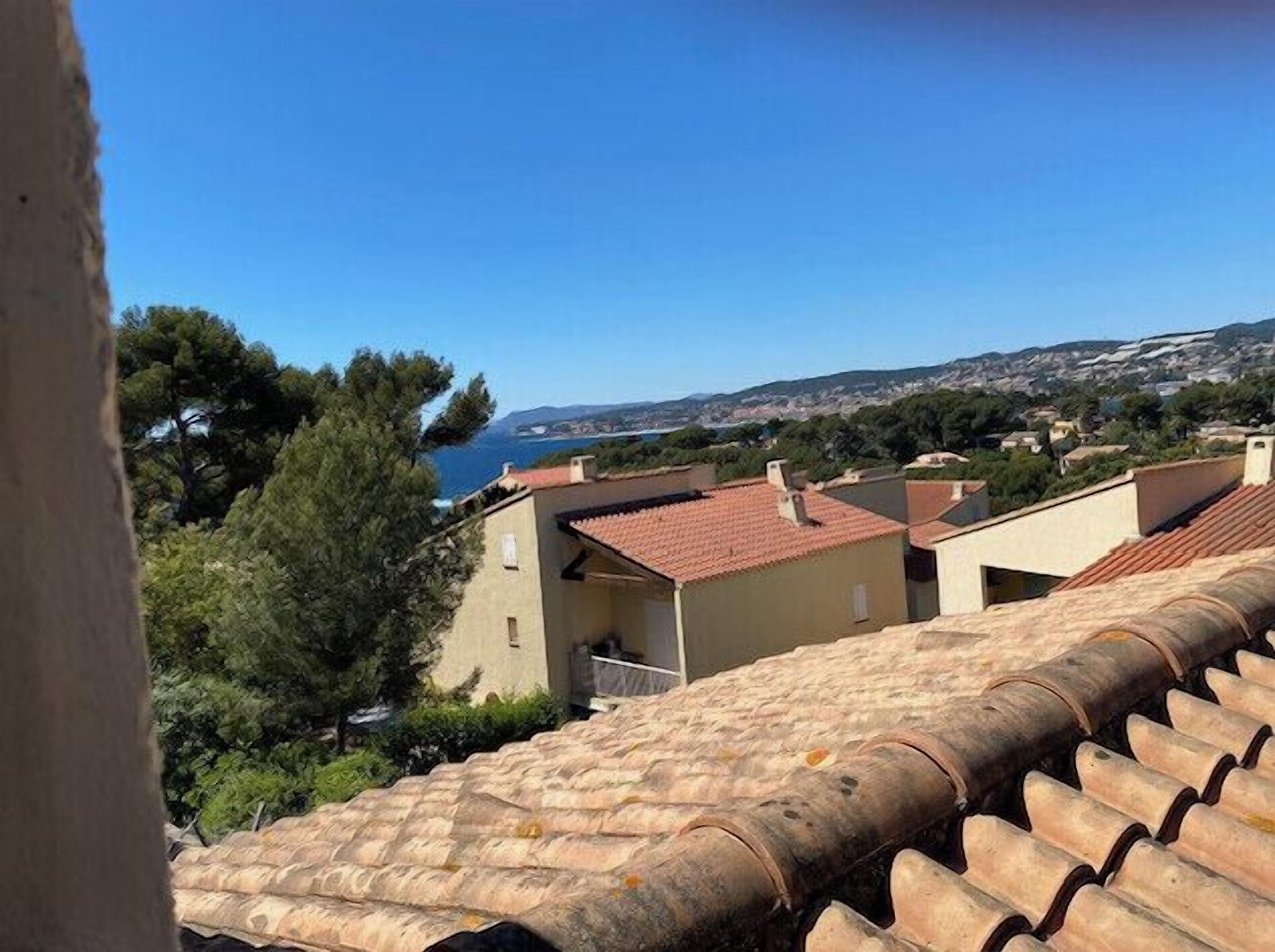 Un pueblo costero con tejados de tejas color terracota, un cielo azul claro y vistas al mar.