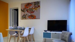 A modern living room with a dining area, a flat-screen TV, and a colorful abstract painting on the wall.
