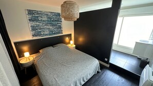 A modern bedroom with a large bed, two bedside lamps, a wall-mounted artwork, and a window with a view.