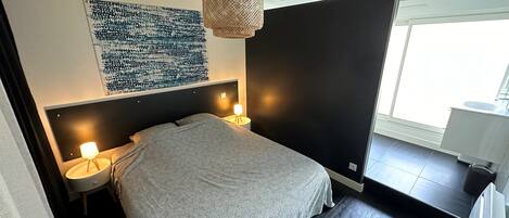 A modern bedroom with a large bed, two bedside lamps, a wall-mounted artwork, and a window with a view.