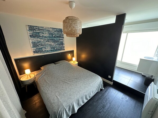 Un dormitorio moderno con una cama grande, dos lámparas de noche, una obra de arte en la pared y una ventana con vistas.