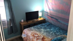 Et soveværelse med en seng, et fjernsyn på et træstel, en lampe og en gardin.