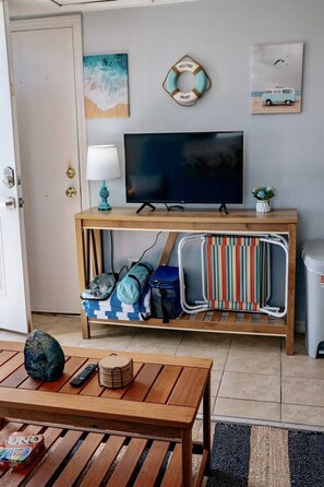 A living area with a TV, a sofa, a coffee table, and a small plant. - Cozy Beach Haven w/Spacious Balcony (Hampton)