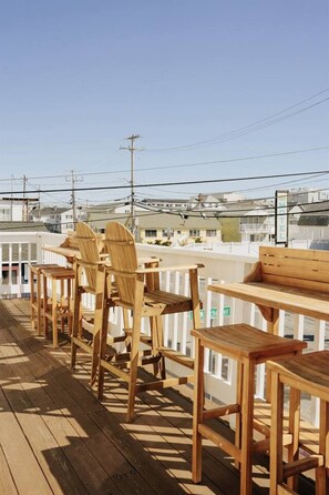 A wooden deck with outdoor seating, including chairs and tables, overlooking a residential area with houses and power lines. - Cozy Beach Haven w/Spacious Balcony (Hampton)