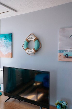 Un soggiorno con televisione a schermo piatto, una decorazione a galleggiante e un quadro a tema spiaggia.