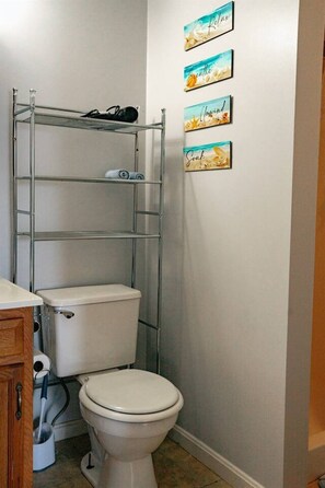 Ein Badezimmer mit Toilette, einem Metallregal und drei Wandbildern.