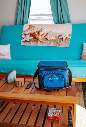 Ein Zimmer mit einem Türkis-farbenen Sofa, einem blauen Rucksack auf einem Holztisch, einer Fernbedienung, einem Stein und einer Packung Snacks.