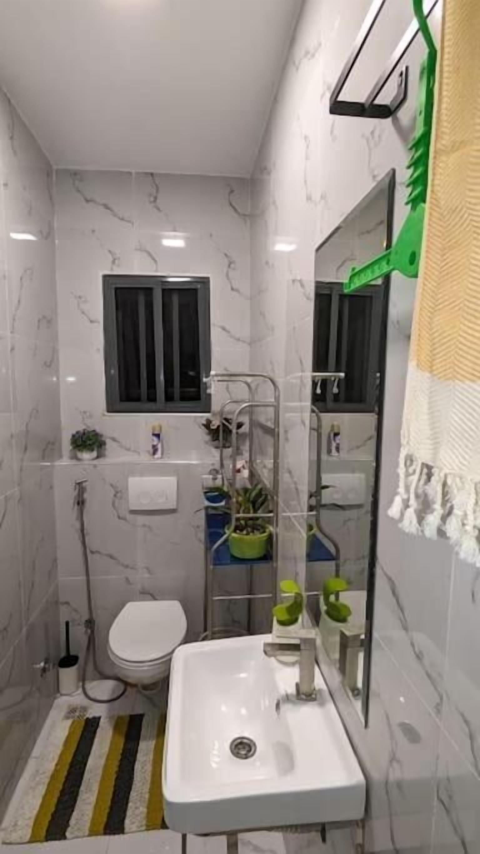 Casa de banho moderna com uma sanita, uma pia branca e uma zona de duche. Há uma janela sobre a sanita e um porta-toalhas na parede.
