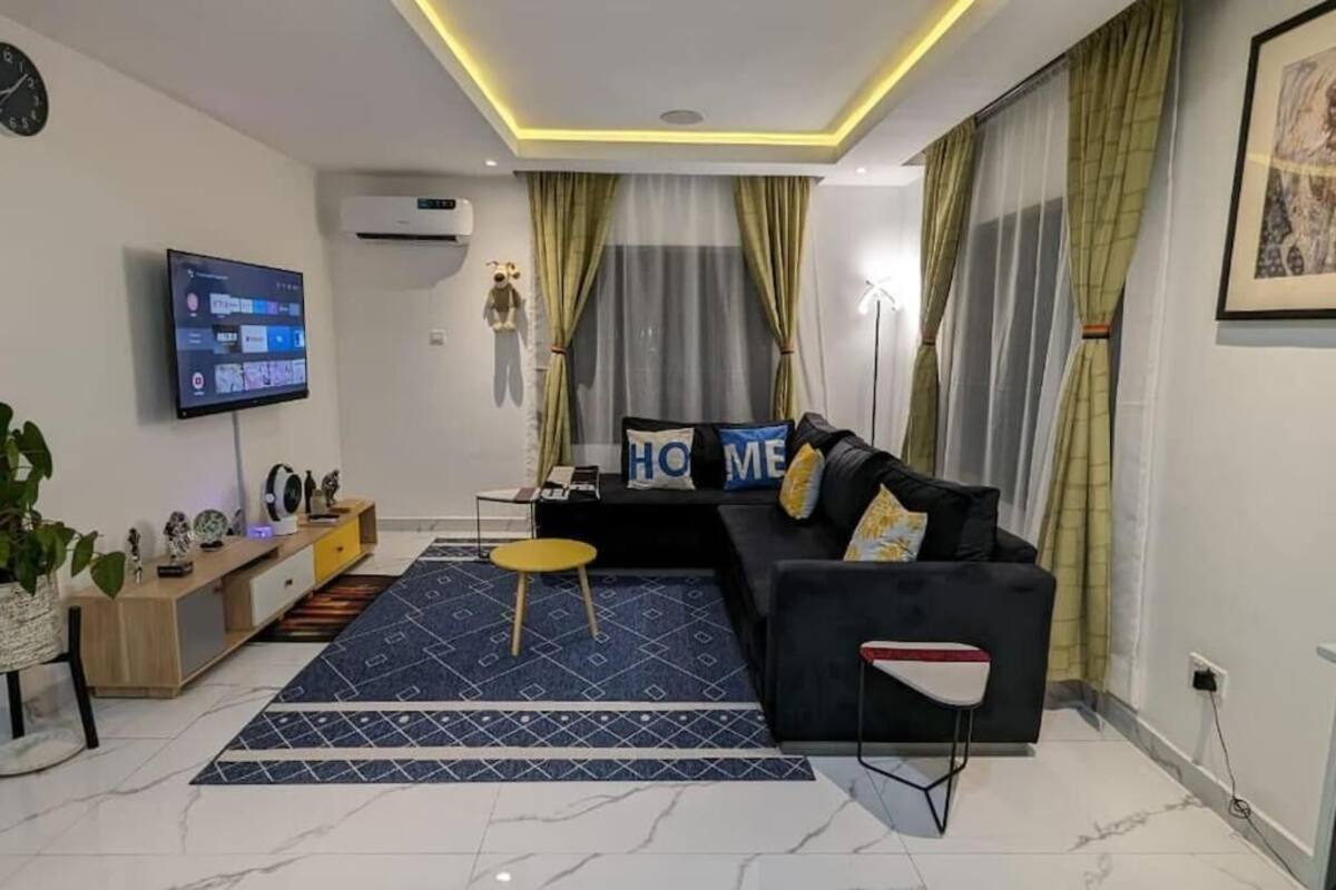 A modern living room with a black sofa, a small round table, a TV mounted on the wall, and a patterned rug.