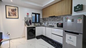 A modern kitchen with white cabinets, a stainless steel refrigerator, a washing machine, and a tiled backsplash. - Micasa-Sucasa Hotel and Suites (Port Harcourt)