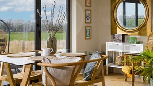 A dining area with a glass table, wooden chairs, and a view of the outdoors. - Heron's Nest -  Ripple, Gloucester, Tewkesbury, sleeping two guests (Ripple)