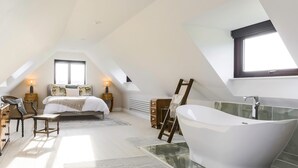 A spacious attic bedroom with a large bed, a white bathtub, and a skylight. - Heron's Nest -  Ripple, Gloucester, Tewkesbury, sleeping two guests (Ripple)